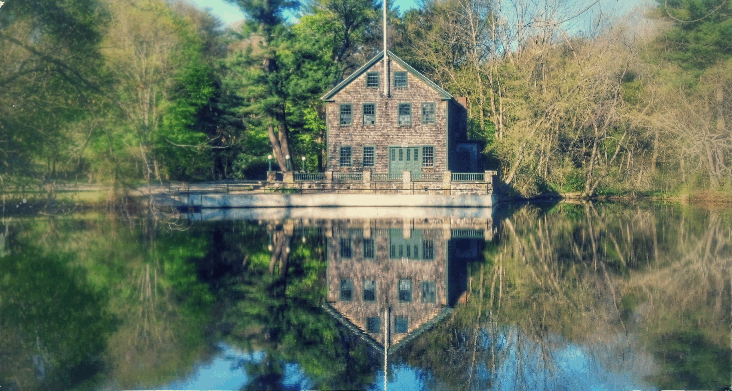 Historic wooden house reflecting in calm water, surrounded by lush greenery, showcasing a serene landscape ideal for outdoor exploration.