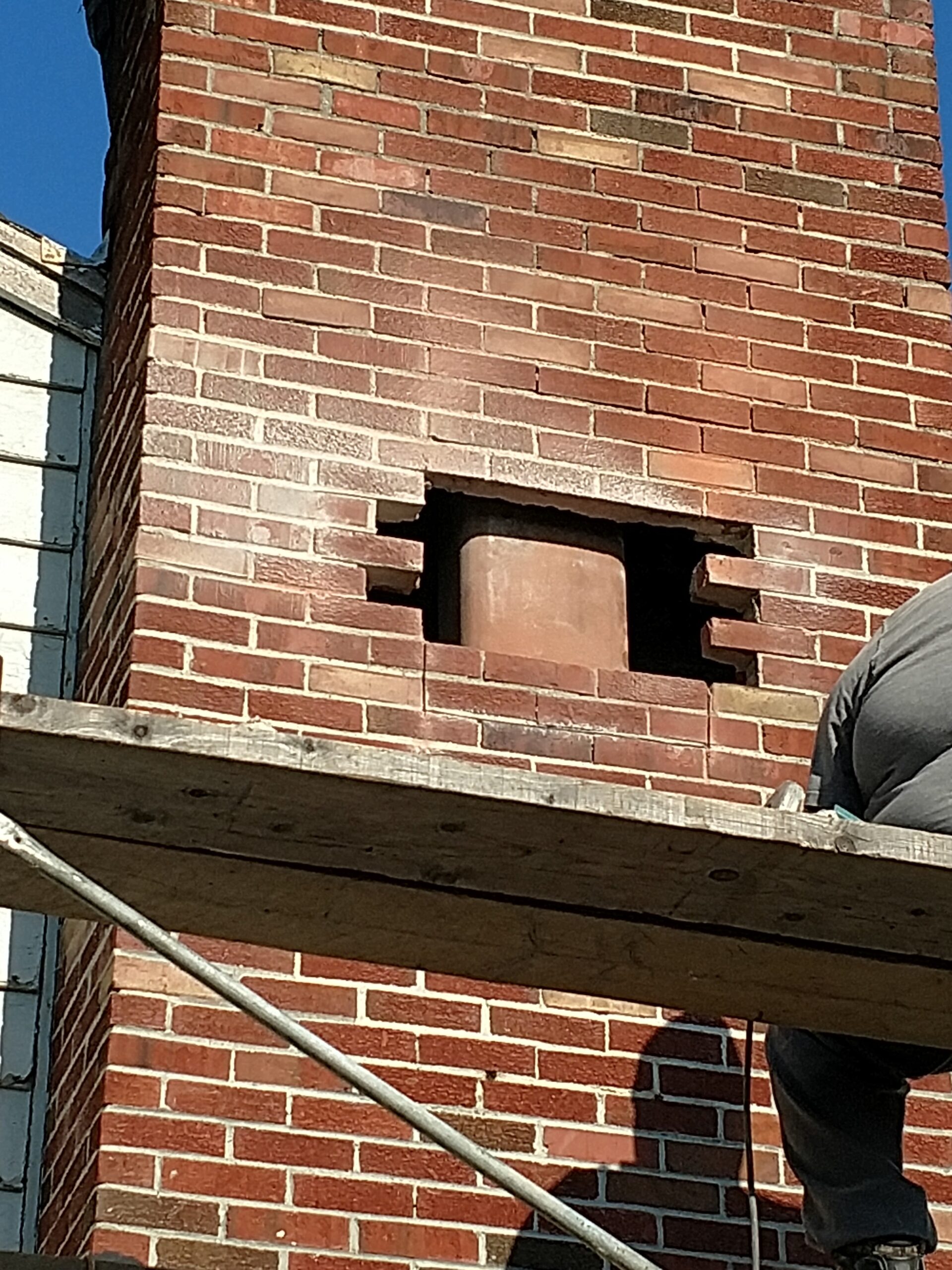 Chimney renovation showing a brick chimney with a cut-out section and scaffolding. Essential for discussing renovation techniques or safety.